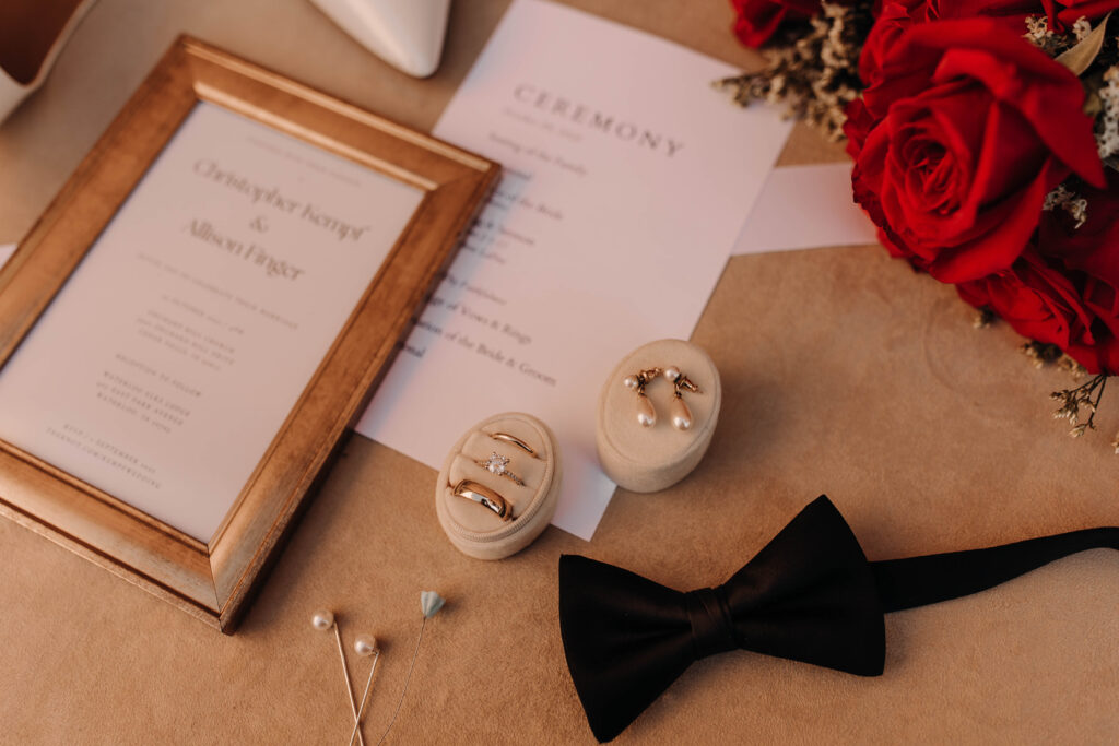 wedding day flat lay with red roses and black bowtie